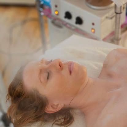 Woman receiving facial steam treatment with eyes closed.