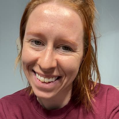 Woman with red hair smiling; wearing a burgundy shirt.