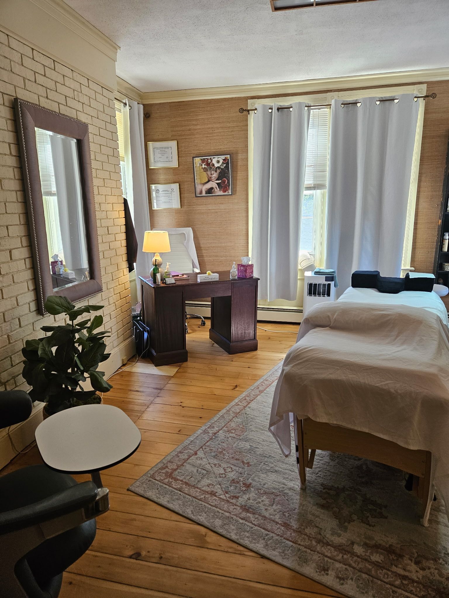 Massage therapy room with two beds, desk, brick wall, and curtains.