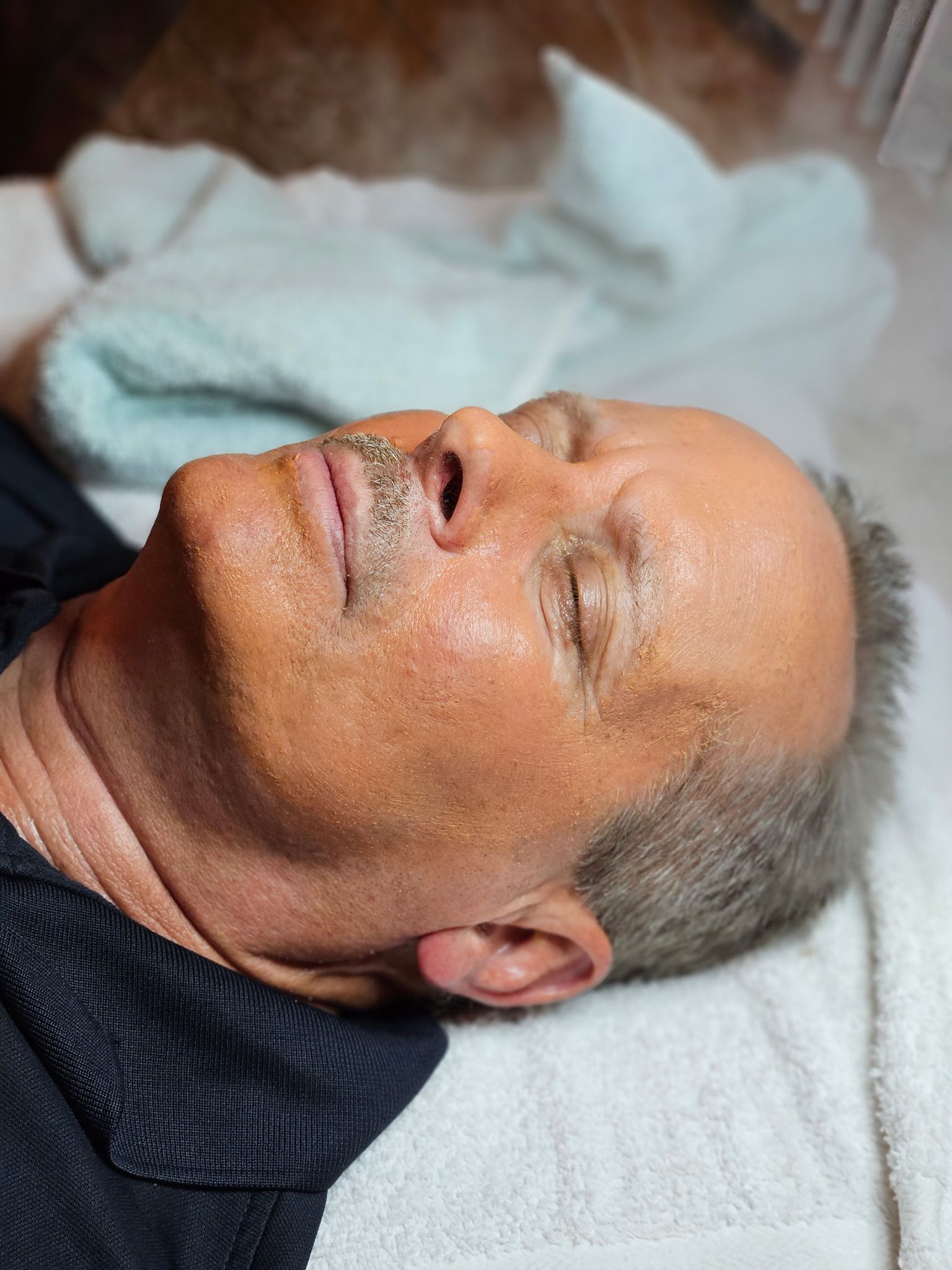Man lying down, face covered in small water droplets, likely receiving facial treatment.