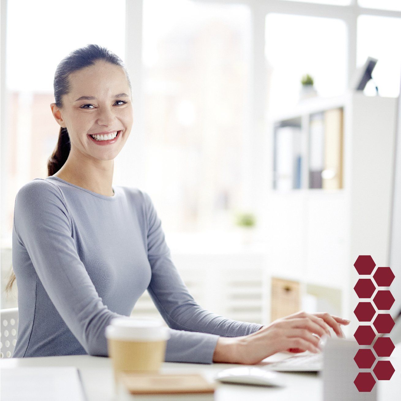 Una mujer sonríe mientras está sentada en un escritorio frente a una computadora.