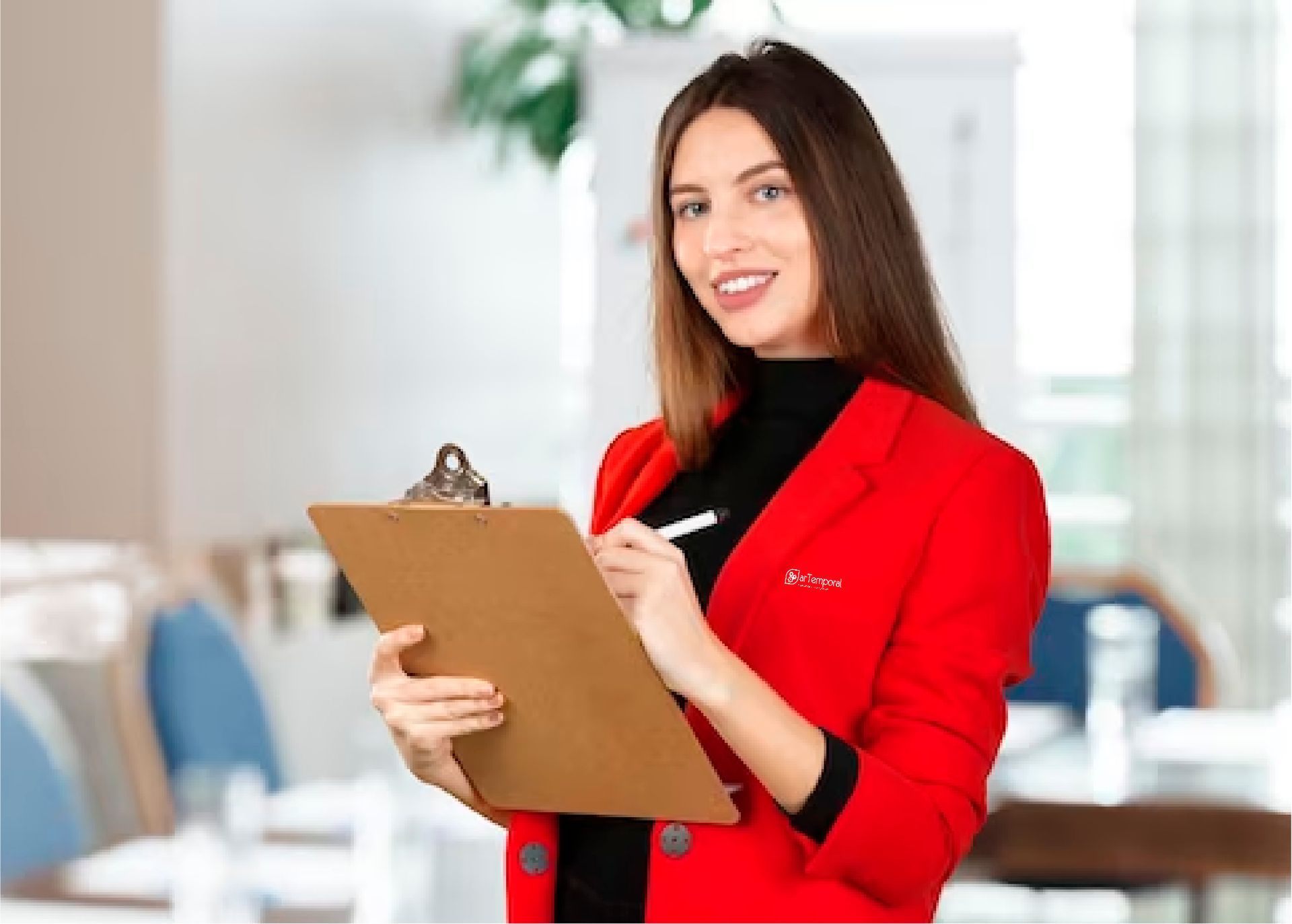 Una mujer con una chaqueta roja sostiene un portapapeles y escribe en él.