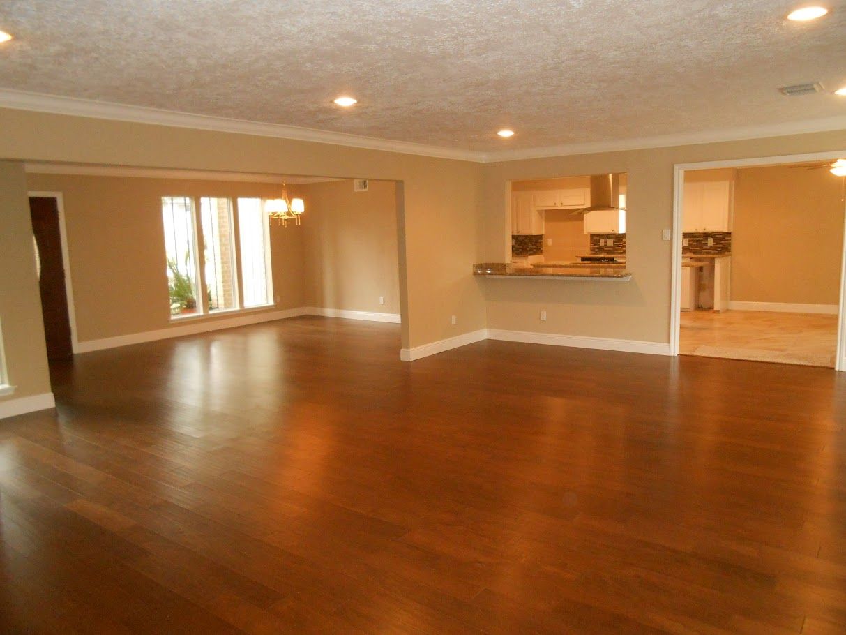 An empty living room with hardwood floors and a kitchen in the background