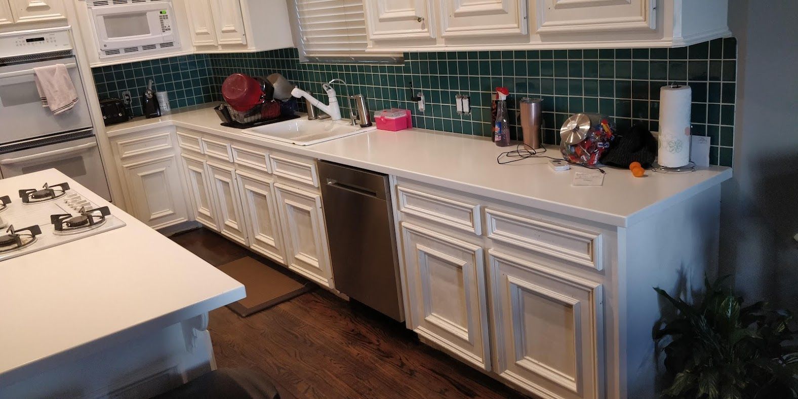 A kitchen with white cabinets , stainless steel appliances , and green tiles.