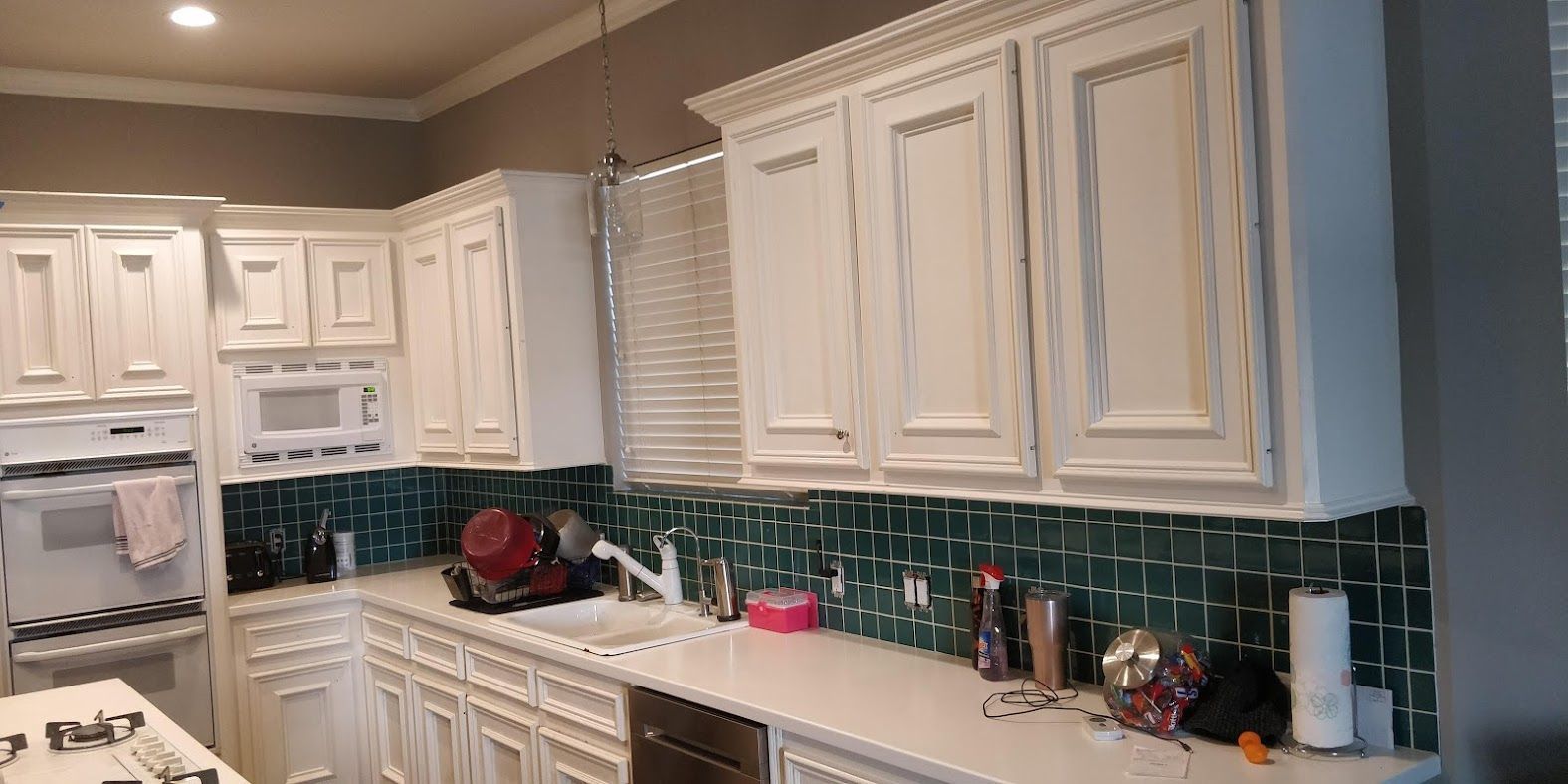 A kitchen with white cabinets and green tiles.