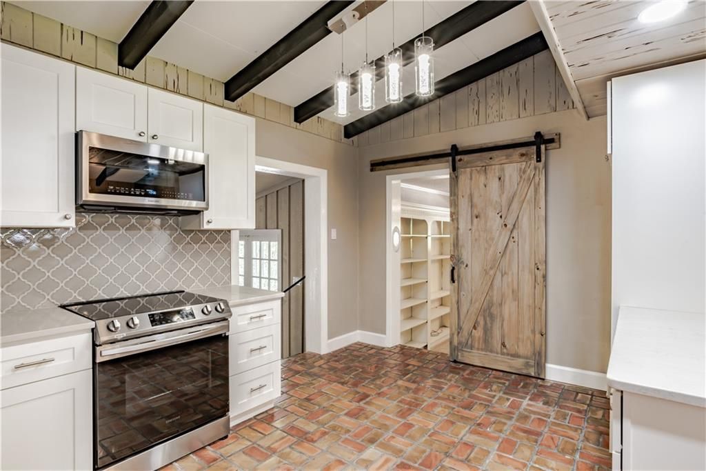 A kitchen with a stove , microwave , refrigerator and sliding barn door.