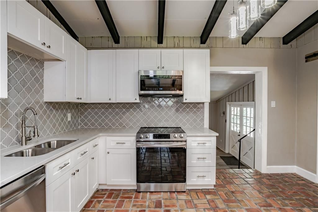 A kitchen with white cabinets , stainless steel appliances , and a brick floor.