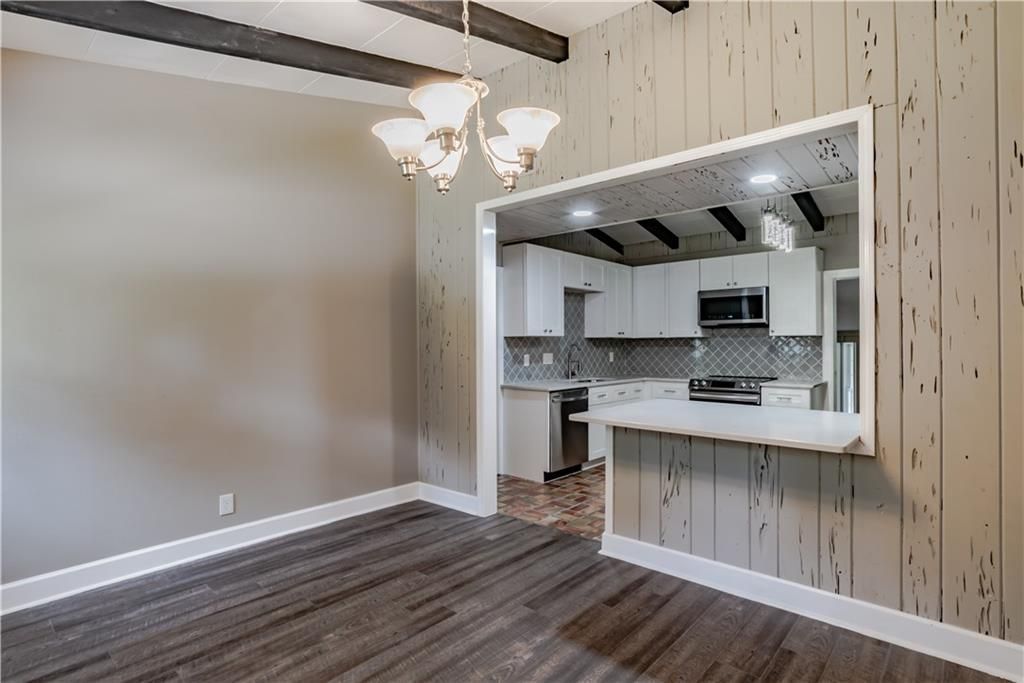 An empty living room with hardwood floors and a kitchen in the background.
