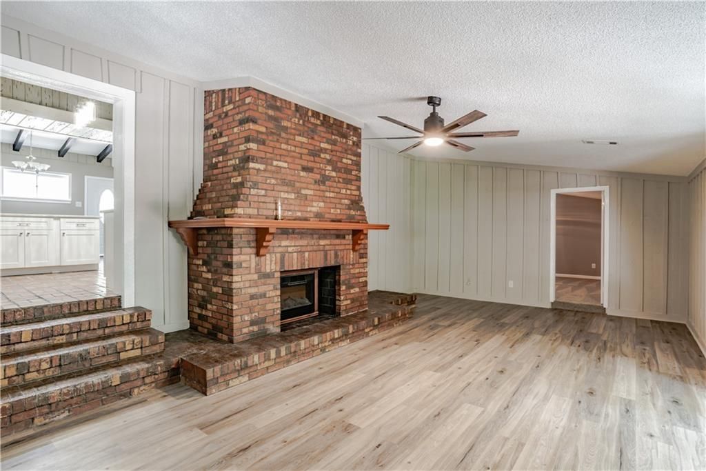 An empty living room with a brick fireplace and a ceiling fan.