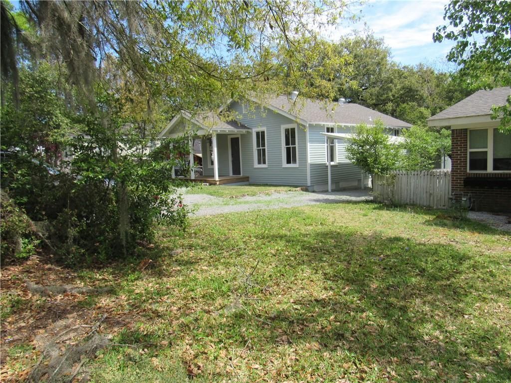 A house with a large lawn in front of it is surrounded by trees and bushes.
