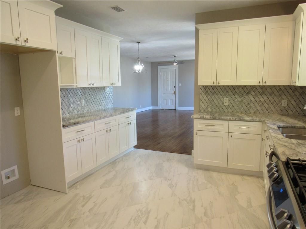 An empty kitchen with white cabinets and granite counter tops.