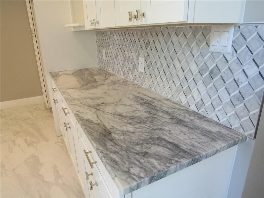 A kitchen with a marble counter top and white cabinets.