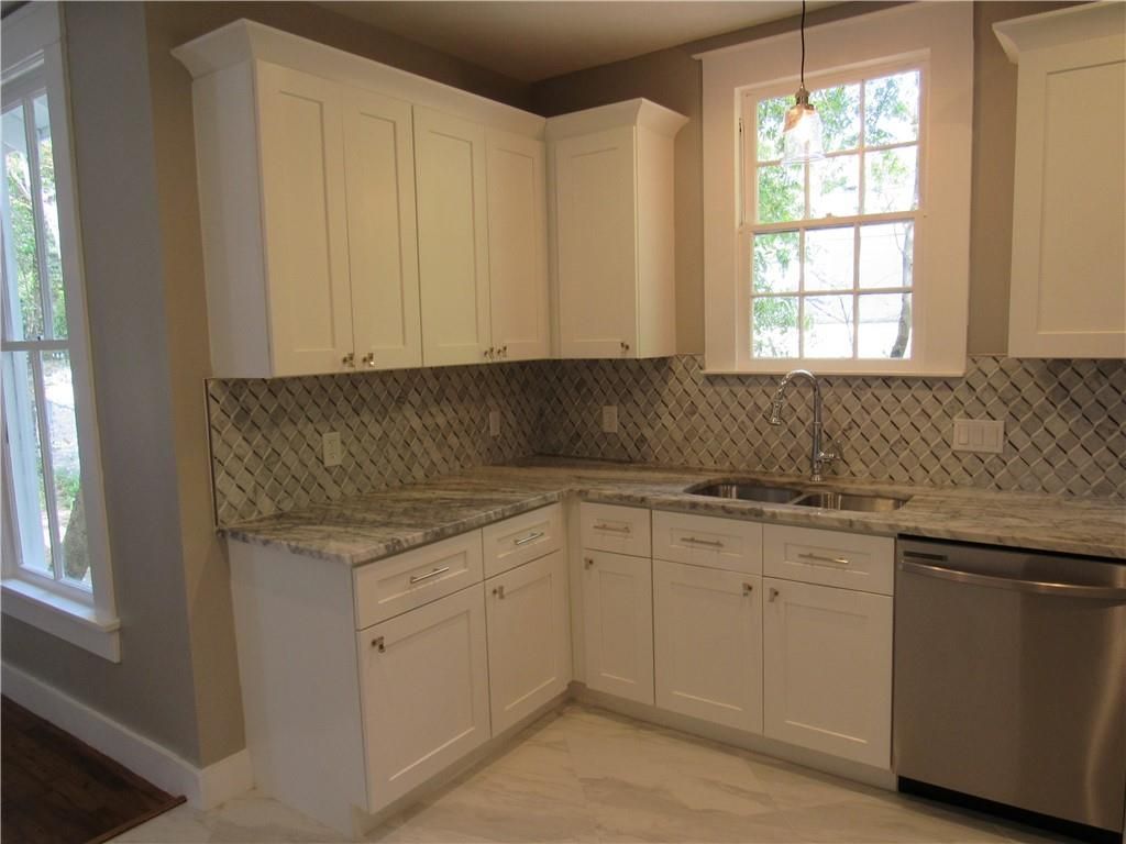 A kitchen with white cabinets , granite counter tops , stainless steel appliances and a window.