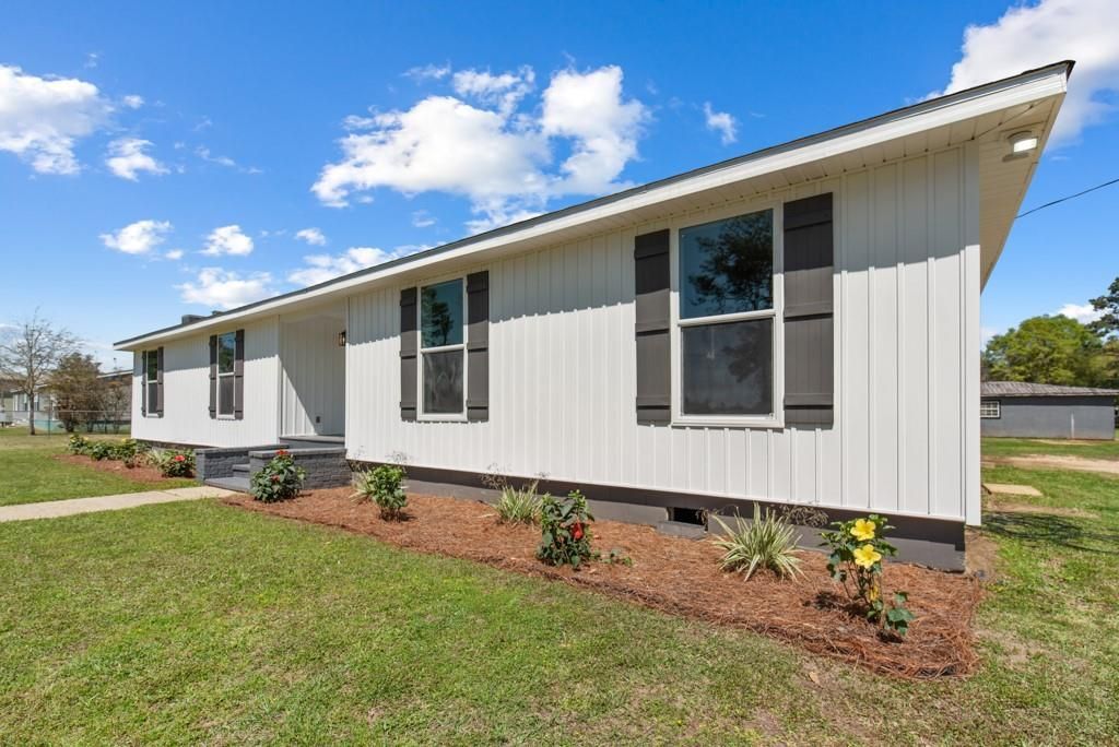A white mobile home with black shutters is sitting on top of a lush green field.