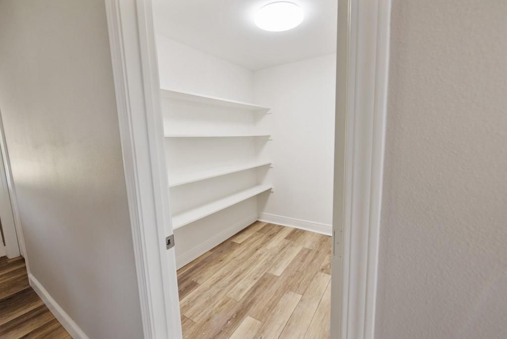 A walk in closet with wooden floors and shelves in a house.