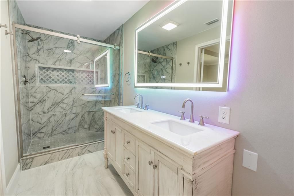 A bathroom with two sinks, a shower and a large mirror.
