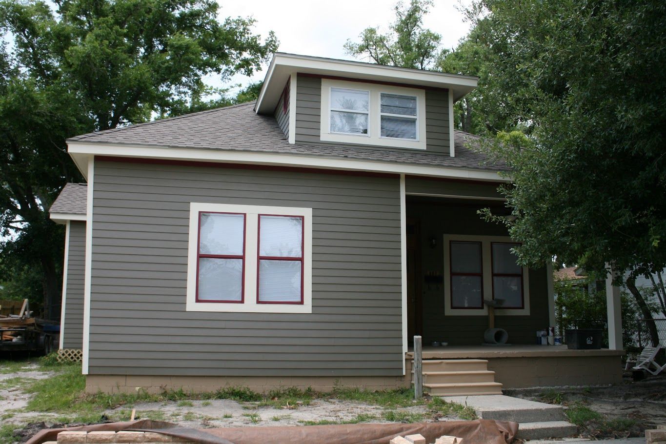 A gray house with a white trim and red windows.