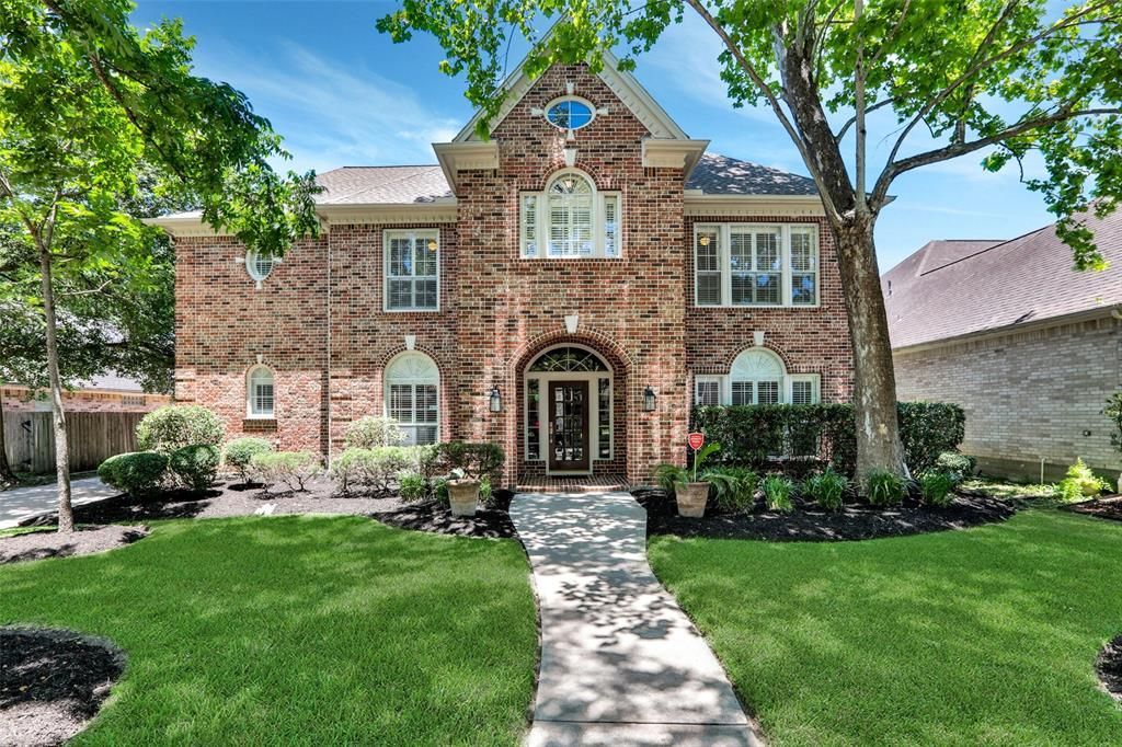 A large brick house with a lush green lawn and trees in front of it.