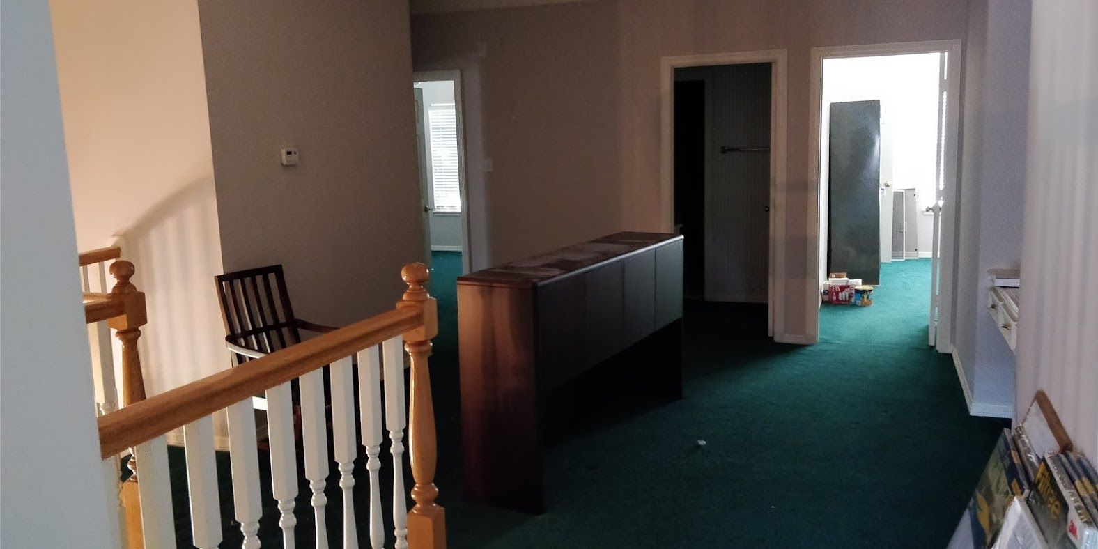 An empty hallway with green carpet and a wooden railing.