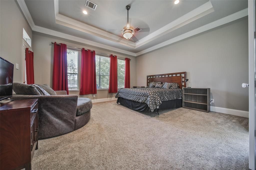 A large bedroom with a bed, a couch, a nightstand, and a television.