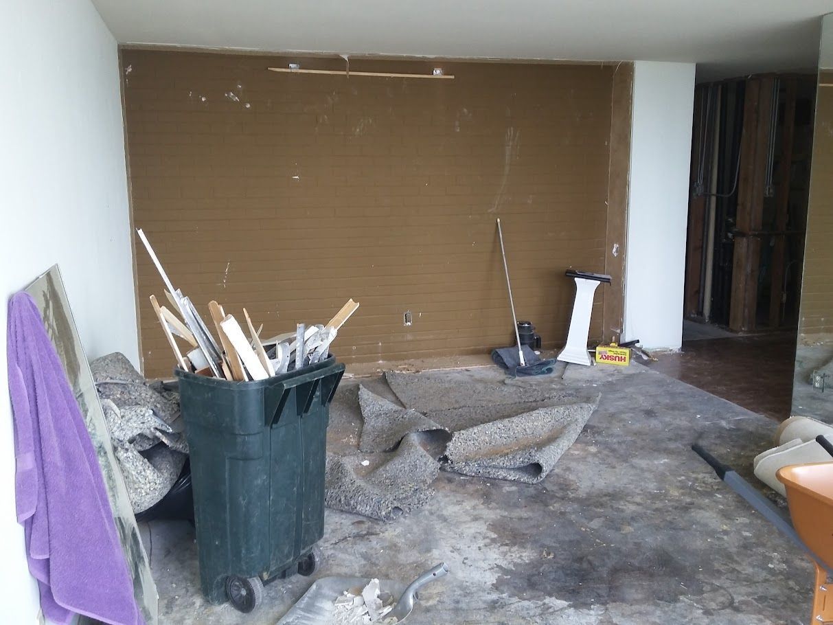 A room with a trash can and a purple towel on the floor.