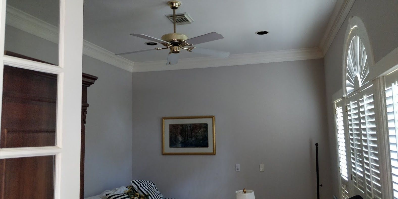 A living room with a ceiling fan and shutters on the windows.