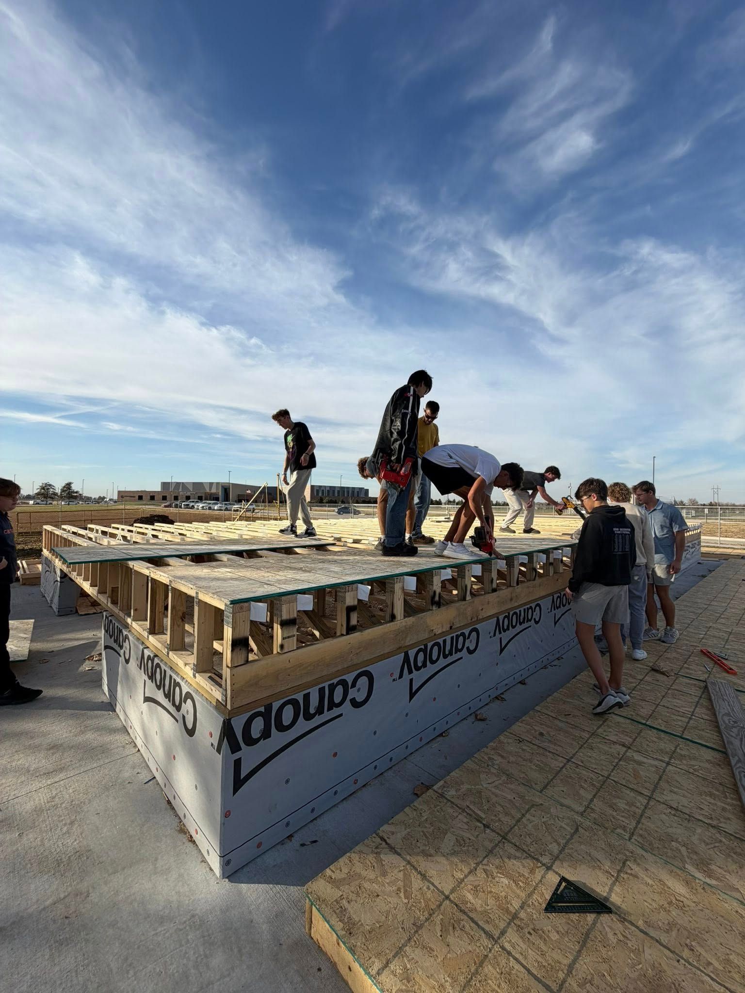 A group works together to assemble the wooden floor framing of a new building on a sunny day.