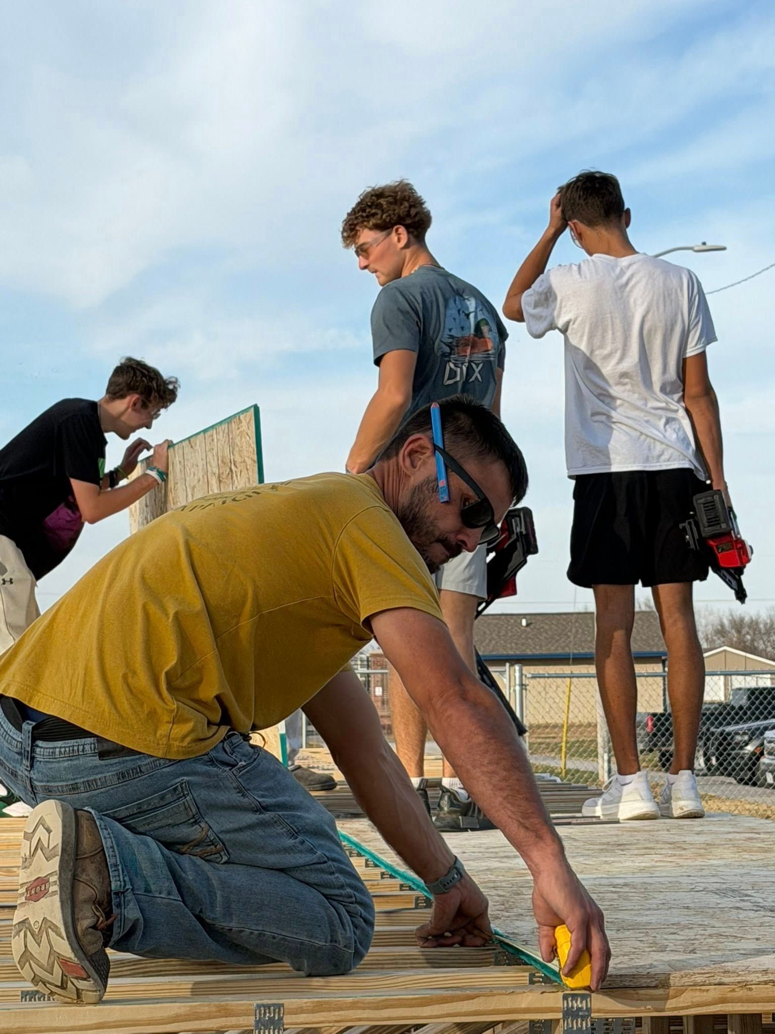 Four people work on a construction site, with one person in the foreground measuring wooden floorboards.