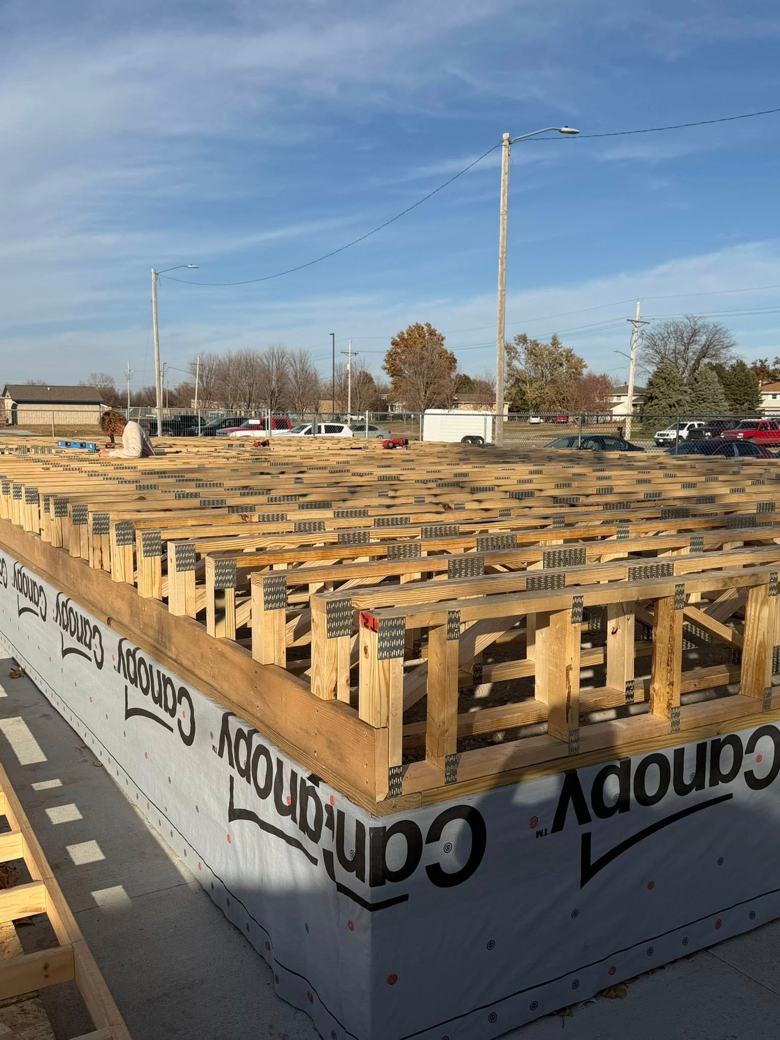 Construction crew installing floor trusses on top of a concrete foundation covered with grey, branded vapor barrier film.