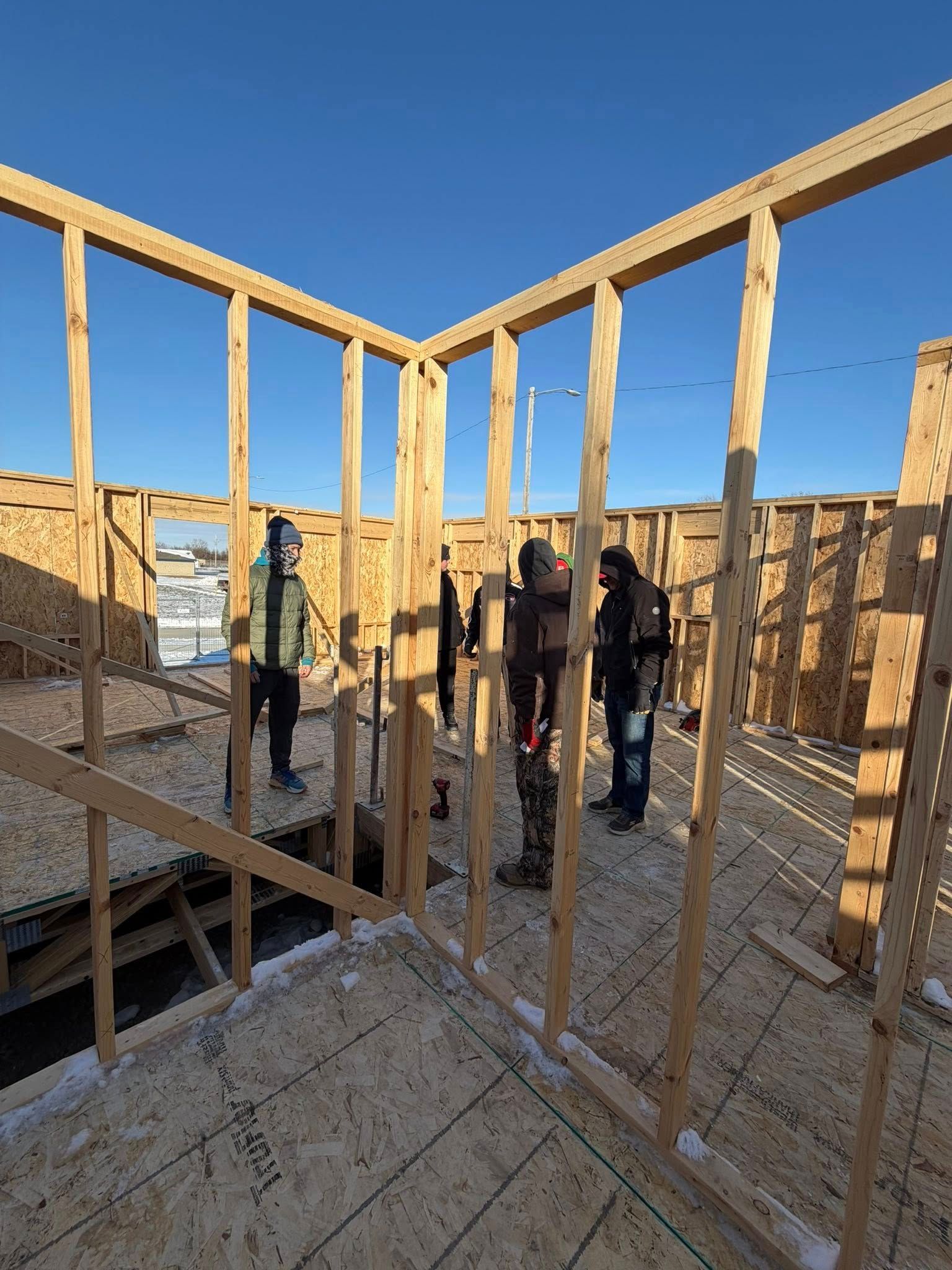 Three construction workers frame the wooden walls of a house under construction on a sunny, clear day.