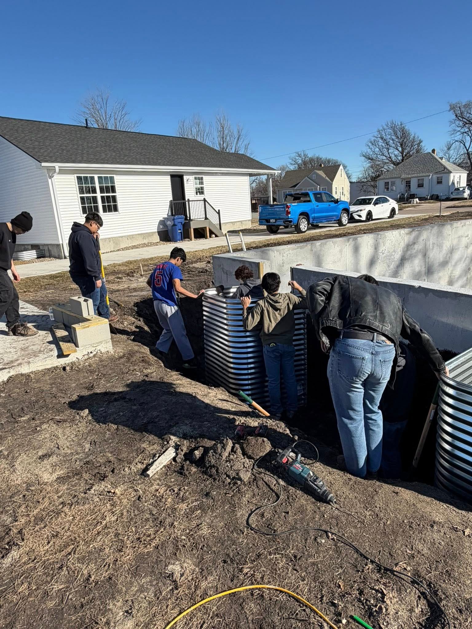 People working to build a raised garden bed with metal sides on a sunny day.
