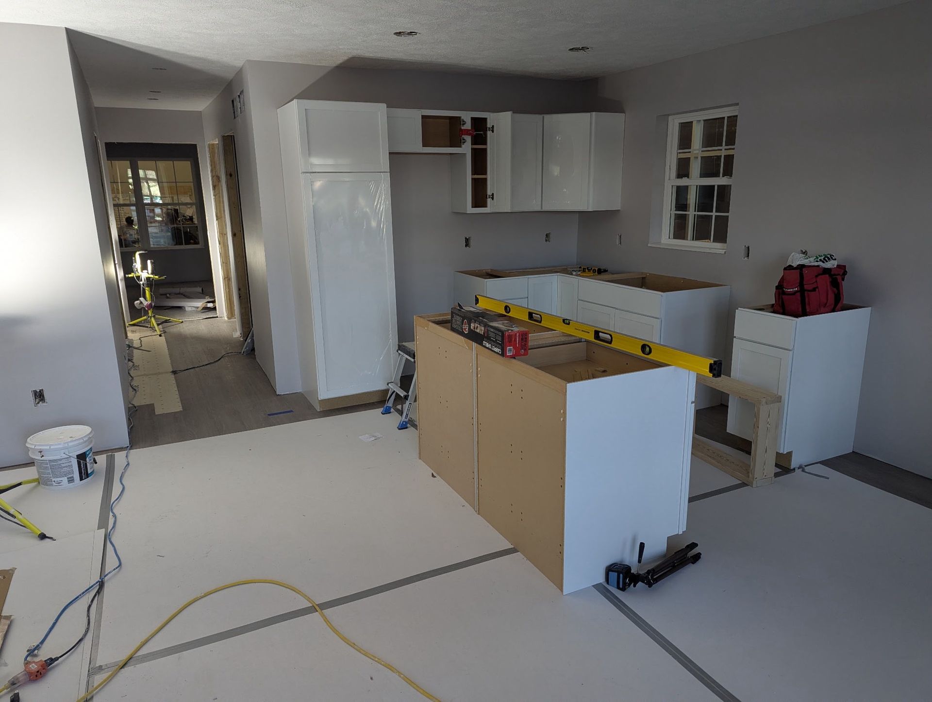 Kitchen renovation in progress with white cabinets, a central island, and a yellow level tool on top.