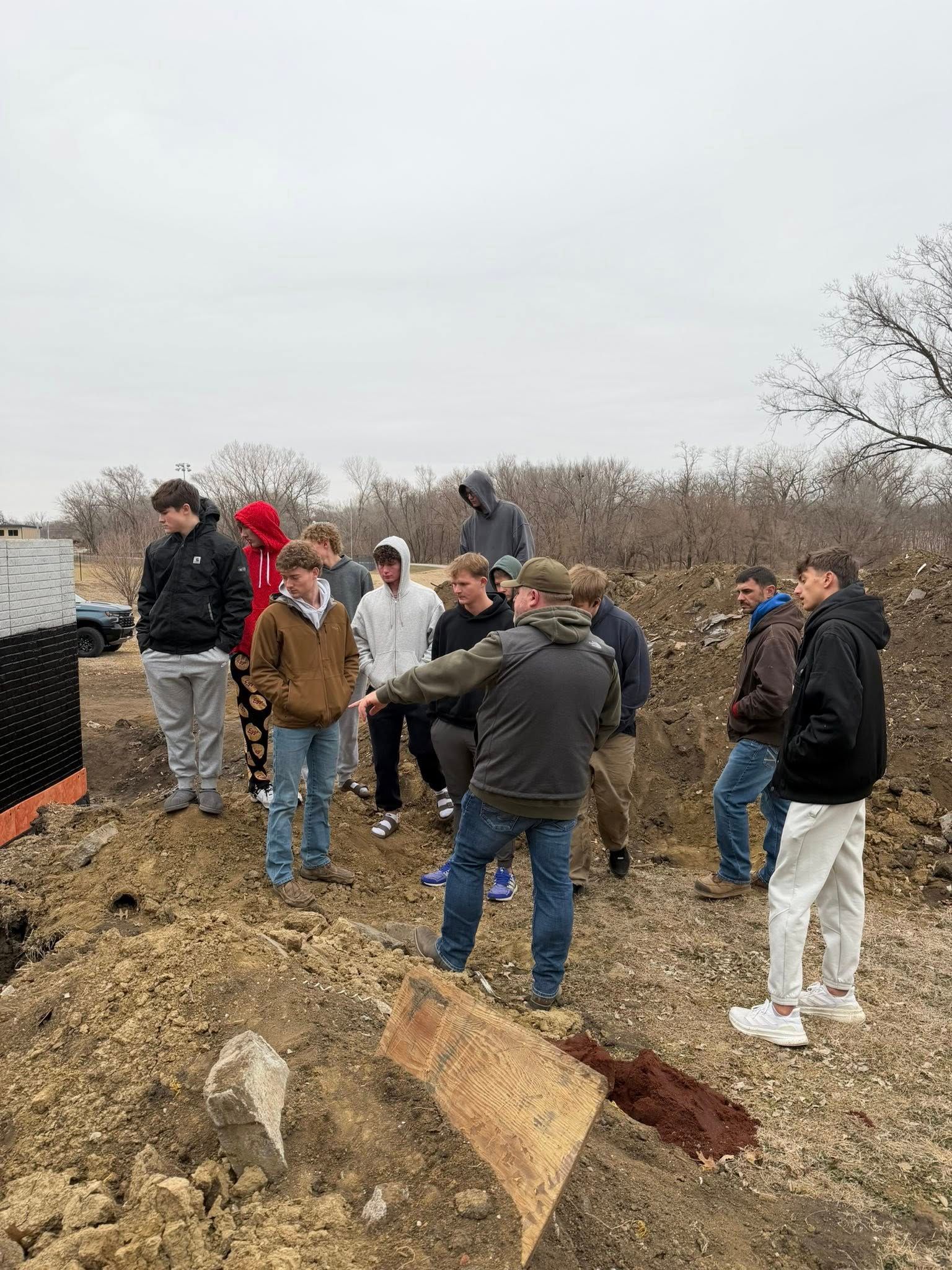 A group of people standing on a construction site, observing an excavation in the dirt.