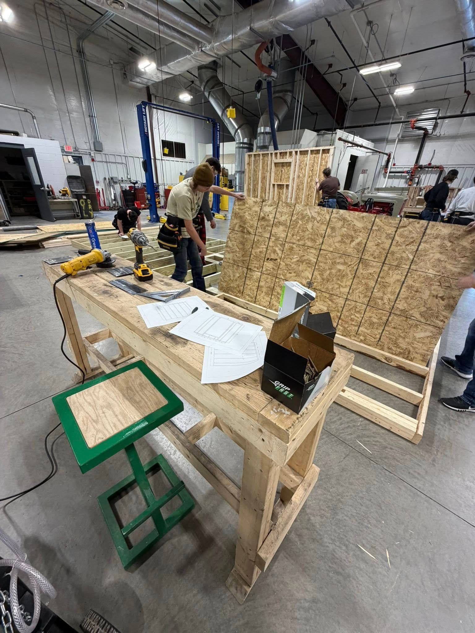 A person in a workshop attaches wood paneling to a frame next to a workbench with tools and supplies.