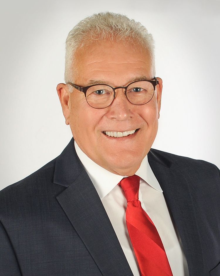 A smiling person wearing a dark blue suit, white shirt, and bright red tie, centered against a plain white background.