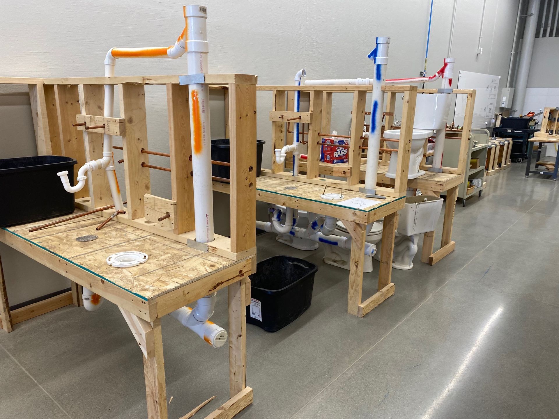 Plumbing training stations: Wooden frames with pipes and fixtures set up in a workshop.