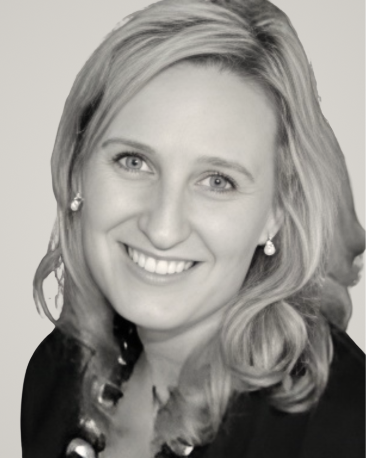 Headshot of a smiling person with wavy blonde hair wearing earrings and a dark top against a light gray background.
