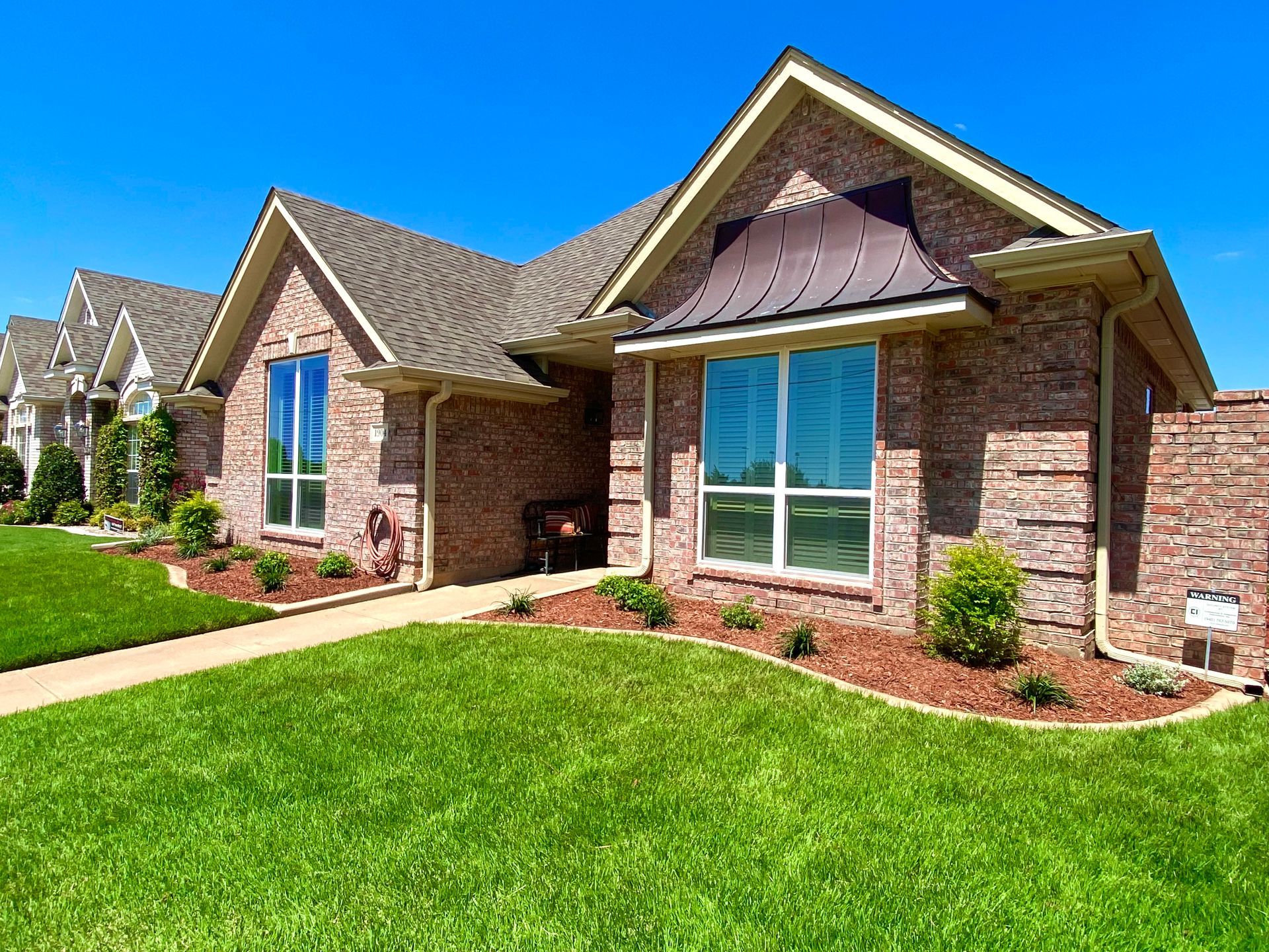 Brick house with brown roof and green lawn on a sunny day.