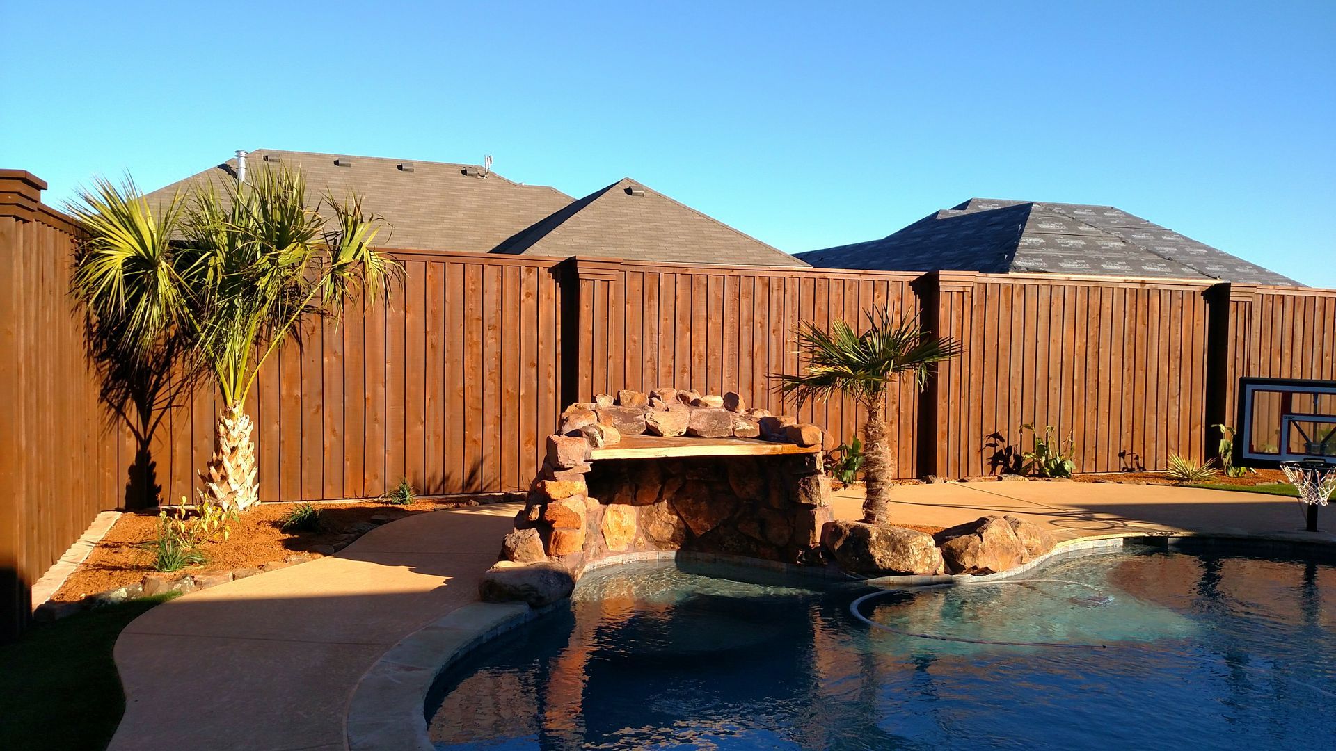 A wooden fence surrounds a swimming pool in a backyard