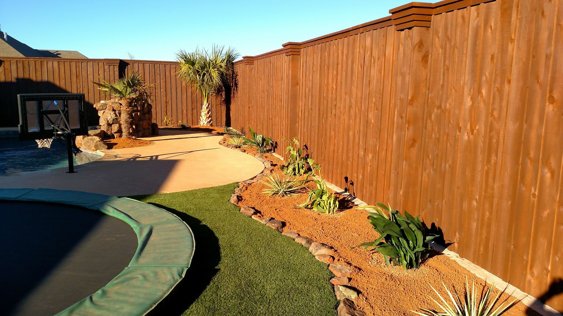 A wooden fence surrounds a trampoline in a backyard.