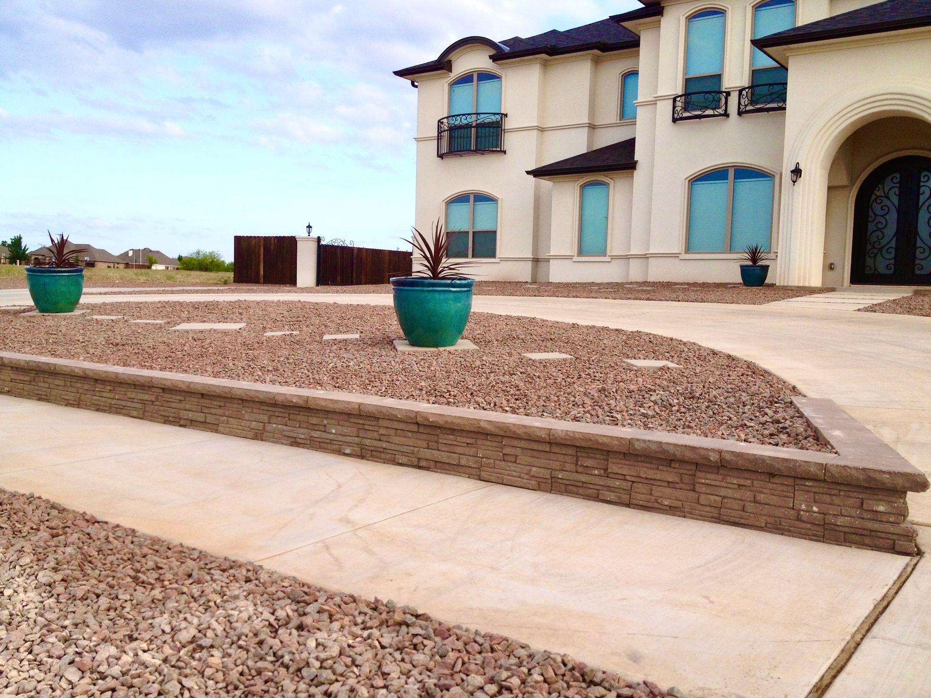 Beige home with a curved driveway, gravel, teal pots, and a stone retaining wall.
