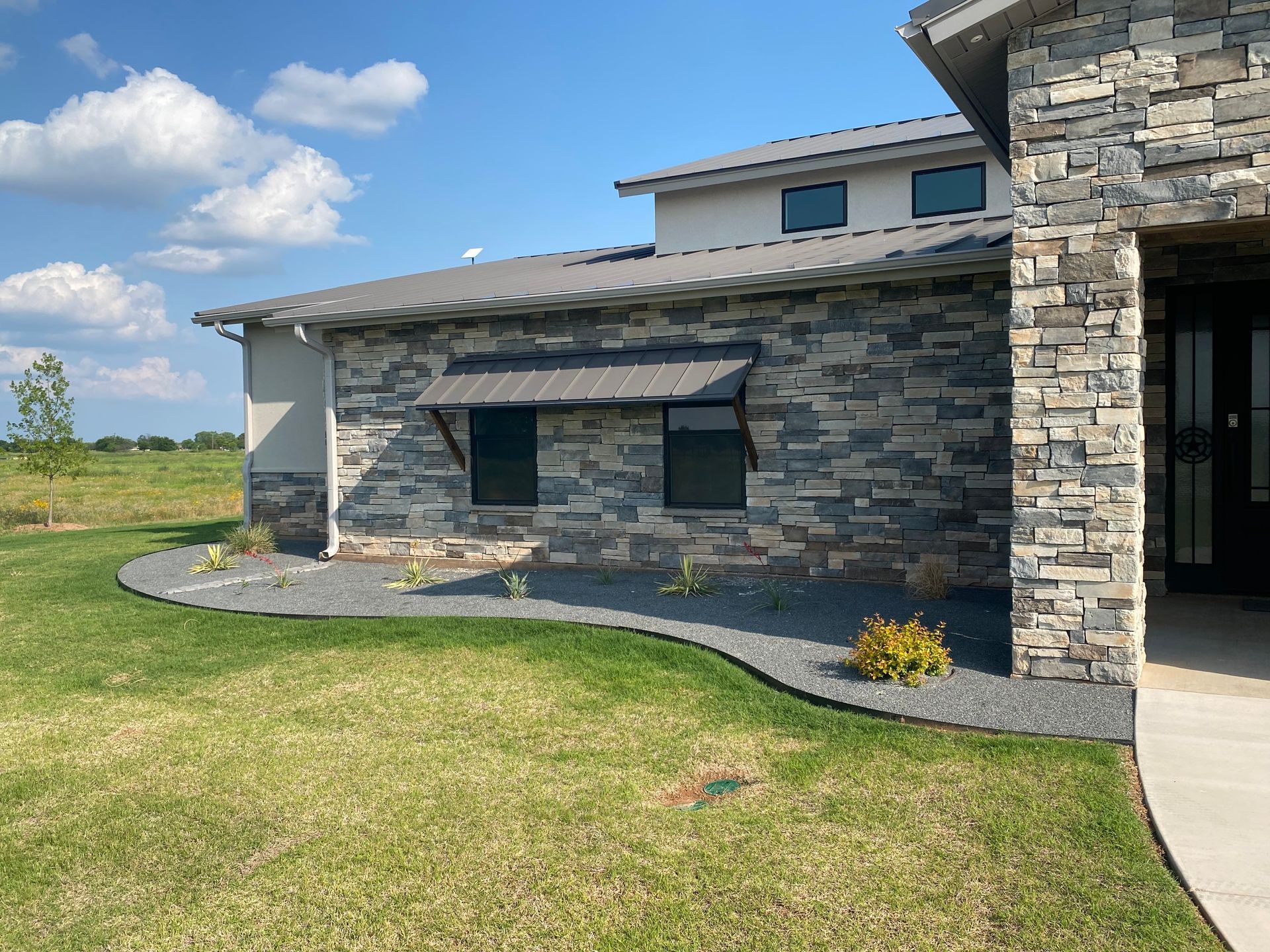 House exterior with stone facade, dark windows, metal awning, and landscaped lawn.