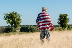 man-camouflage-uniform-holding-american-flag-golden-field-with-green-trees