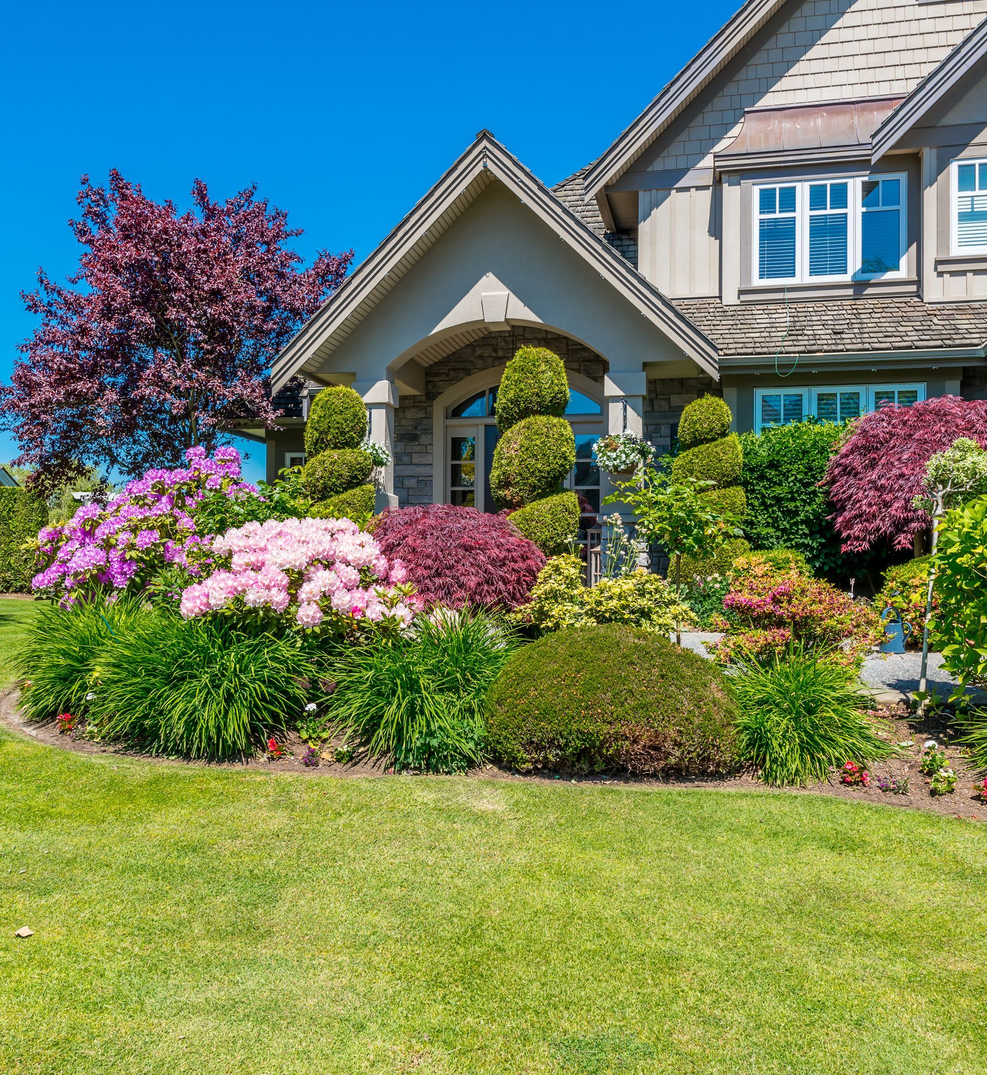 a house with lots of flowers and bushes in front of it