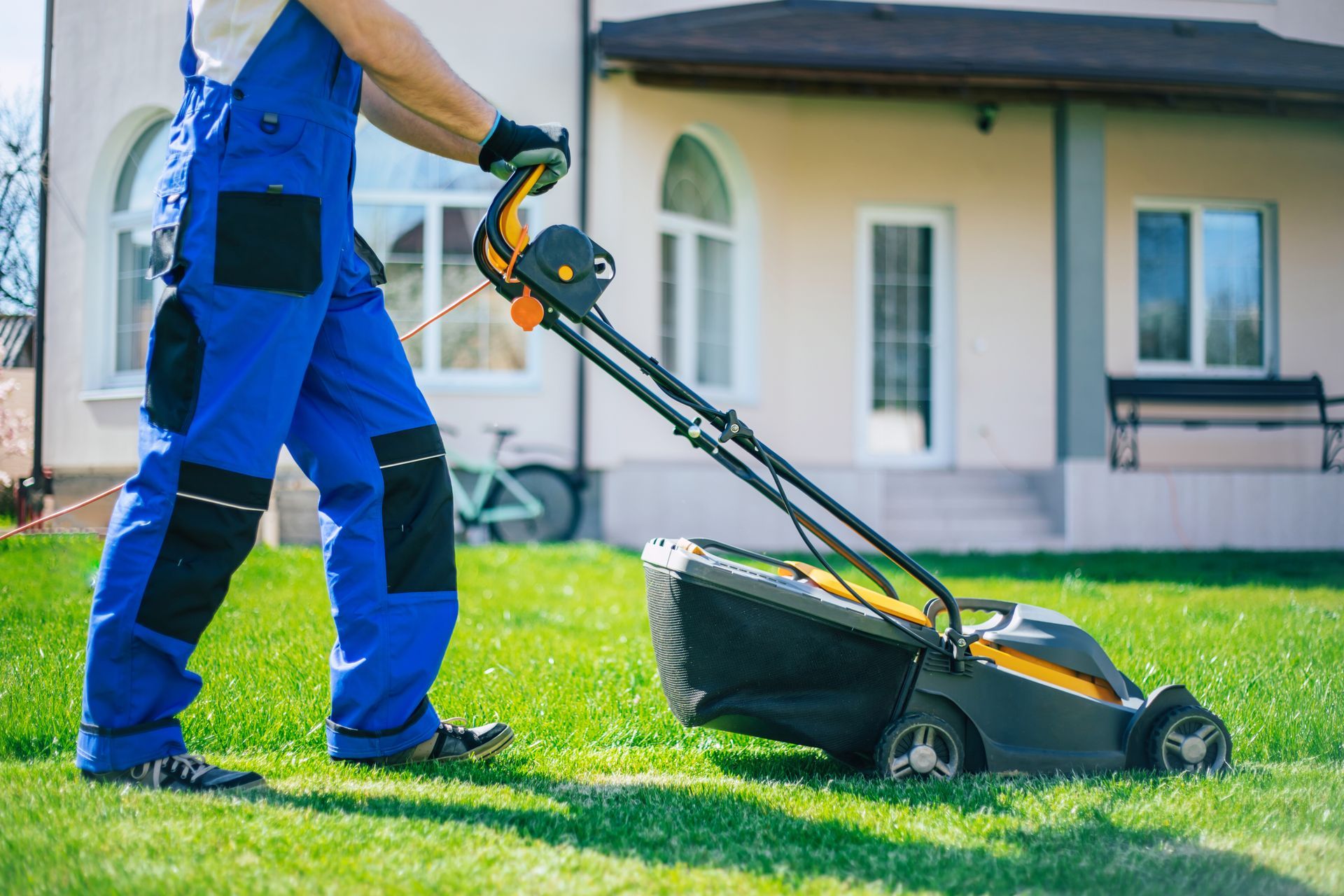 A man is using a lawn mower to cut the grass in front of a house.