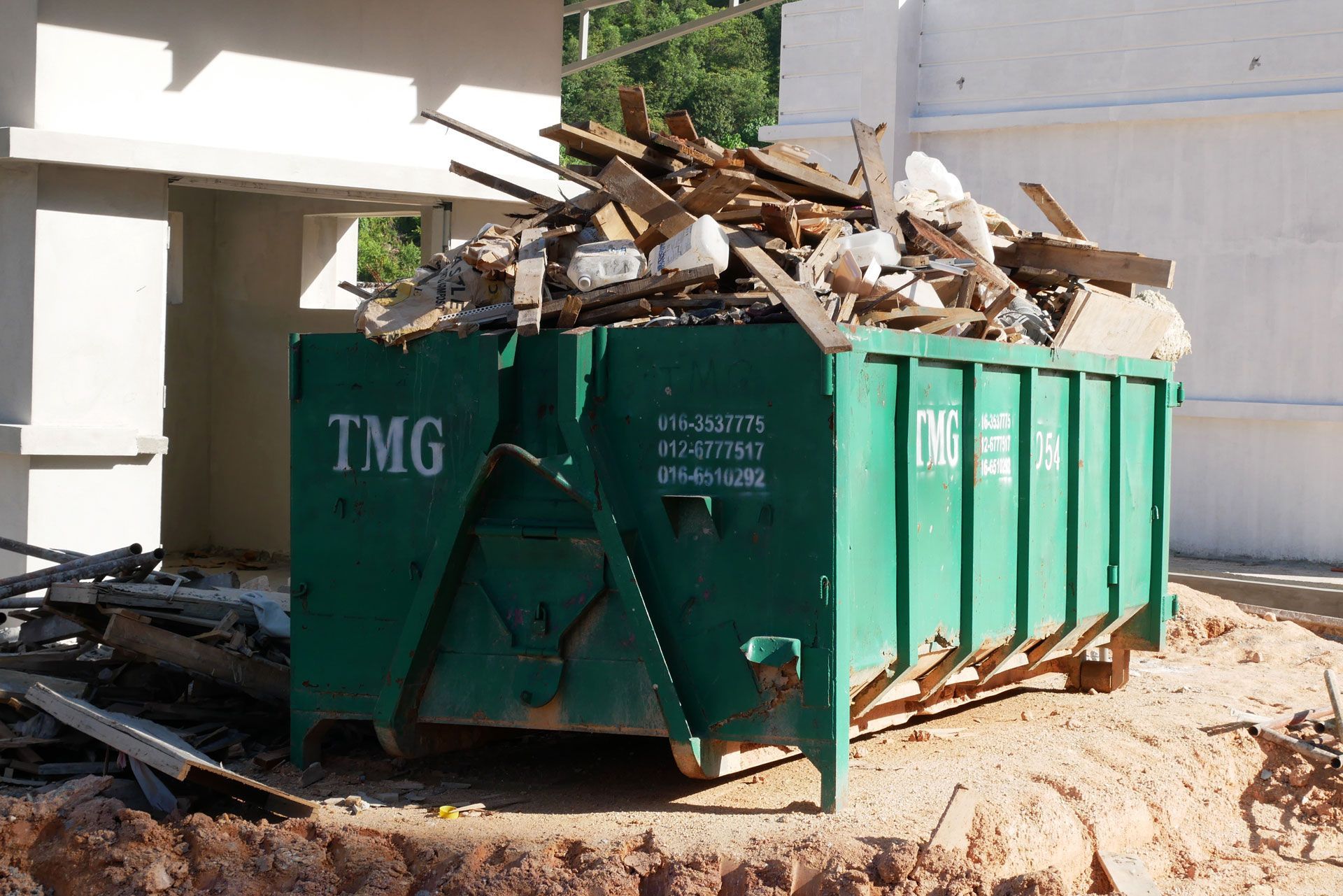 Green dumpster filled with construction debris beside a building under construction