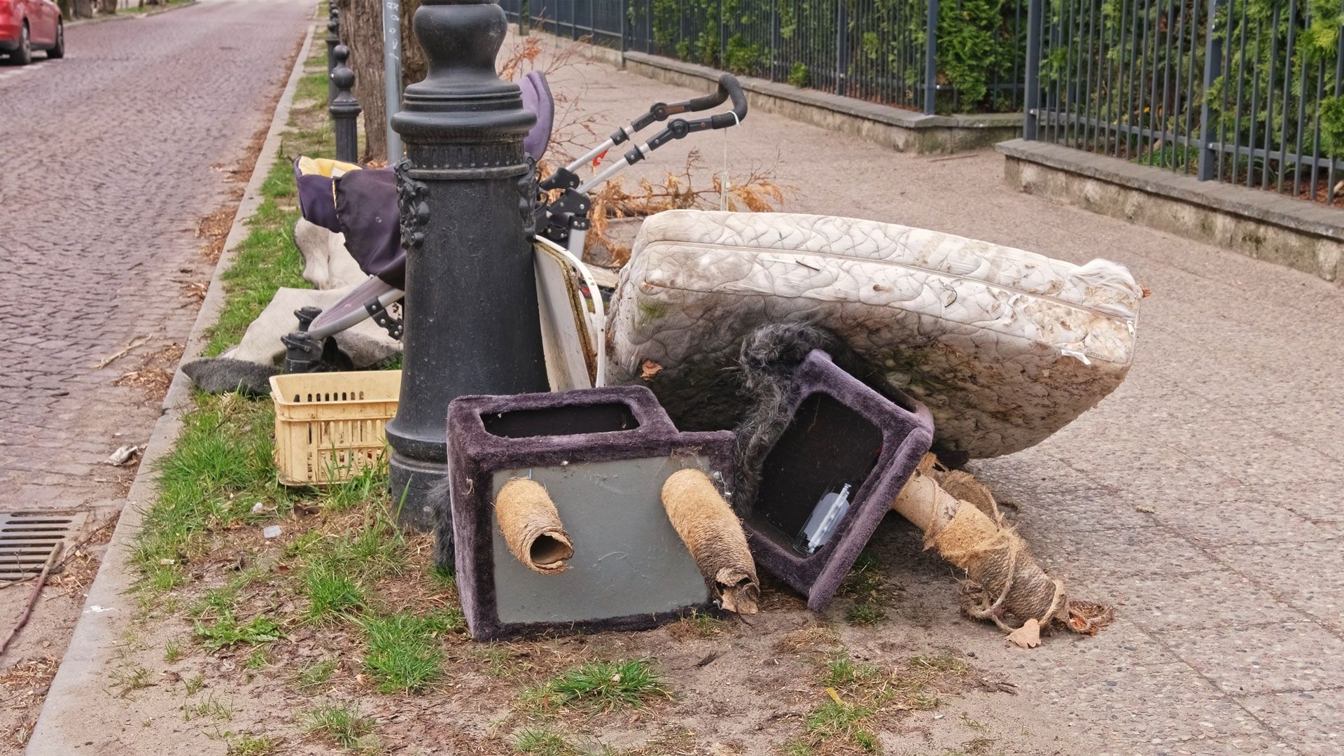 Discarded furniture and debris piled on a sidewalk beside a black lamppost and curb.