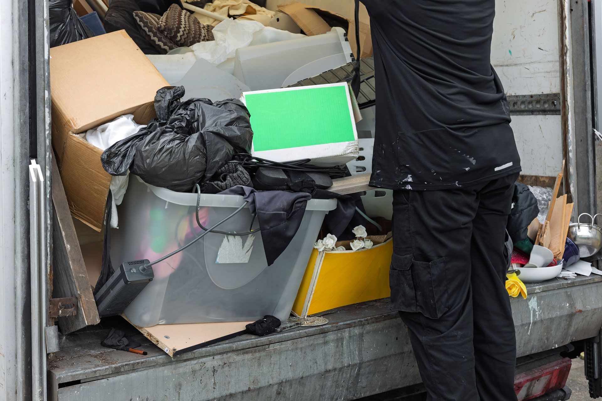 Person loading a truck bed full of cardboard boxes, bags, and assorted household items