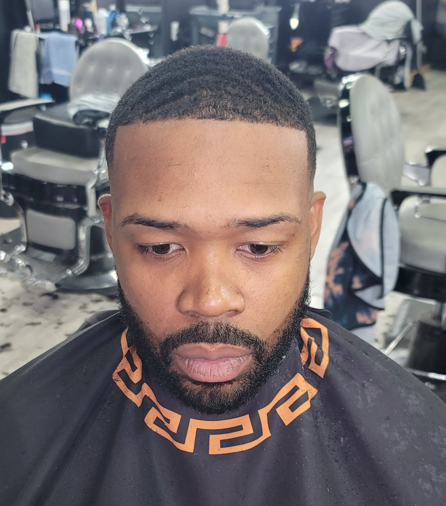 Man in barber chair, dark hair with high fade, full beard, getting a haircut.