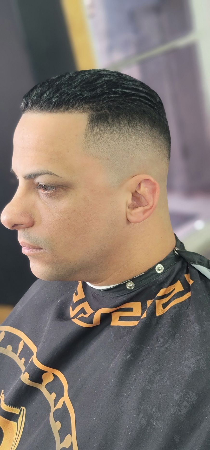 A man with a fade haircut, featuring an intricate design, is in a barber shop.